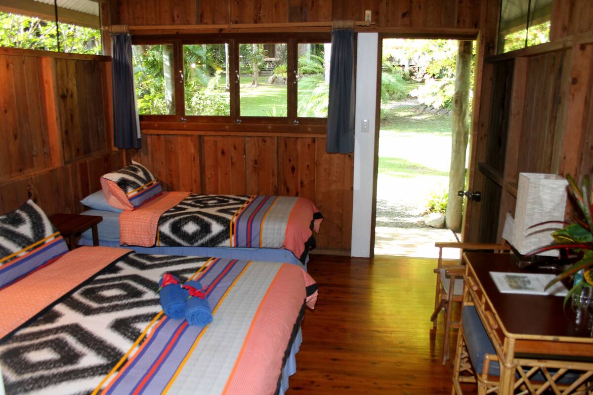 A wooden room with two beds, a table, and a view of a garden.