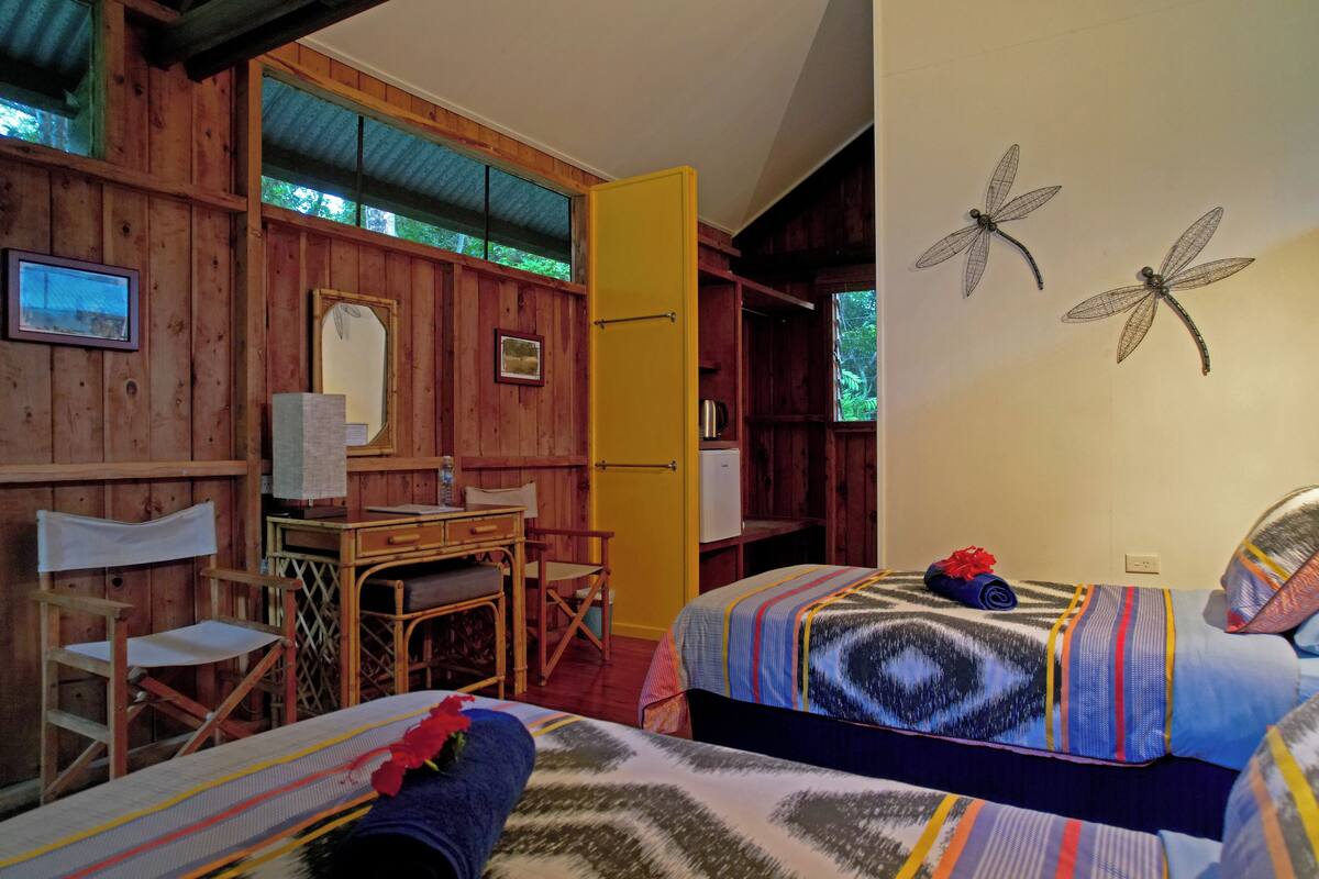 A wooden cabin with two beds, a desk, chairs, and a yellow door.