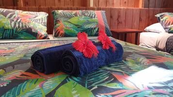 A bed with a rolled-up blue towel and red hibiscus flowers, set against a colorful leaf-patterned bedspread.
