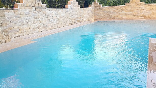 Une piscine aux murs en pierre et à l’eau d’un bleu cristallin.