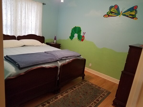 Een slaapkamer met een bed, nachtkastje, lamp en een kapstok.