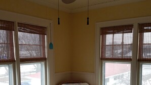 Una habitación de esquina con un sillón de mimbre, una otomana y una mesa de vidrio.