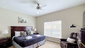 A bedroom with a bed, a nightstand, a dresser, a chair, a ceiling fan, and a window with blinds.