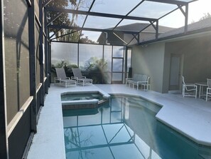 A pool area with a glass enclosure, lounge chairs, and a hot tub.