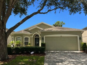 A two-story house with a garage, a driveway, and a large tree in the foreground.
