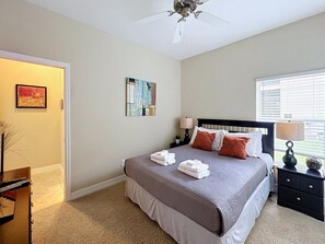 Een slaapkamer met een bed, nachtkastjes, een plafondventilator, kunstwerken aan de muur en een raam met zonwering.