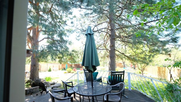 En terrasse med et rundt bord og stole, en grøn parasol og et hvidt gelænder.
