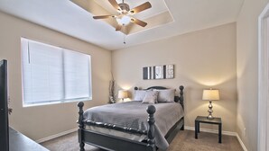 A bedroom with a bed, a ceiling fan, a nightstand, a lamp, a TV, and a window with blinds. - La Cueva~fantastic 3 Bedroom Home. Sleeps 6-8 People. Near Carlsbad Caverns (Carlsbad)