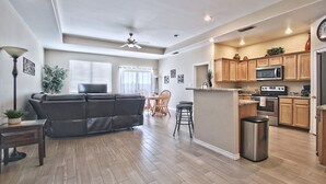 A spacious living room with a black leather sofa, wooden dining table, and chairs. A kitchen area with wooden cabinets and modern appliances is visible. - La Cueva~fantastic 3 Bedroom Home. Sleeps 6-8 People. Near Carlsbad Caverns (Carlsbad)
