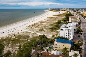 An aerial view of a coastal area with a beach, buildings, and a road.