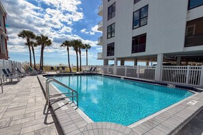 A swimming pool with lounge chairs and palm trees, surrounded by a white fence.