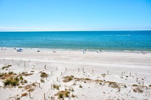 A wide sandy beach with a clear blue ocean, a few people, and some beach umbrellas.