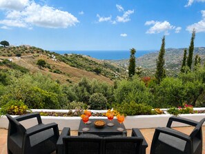 A terrace with wicker furniture, a table with drinks and a bowl of nuts, and a scenic view of the sea and hills. - Sun-kissed Exclusive Villa Retreat with Private Pool, Panoramic Sea Views & AC (Frigiliana)