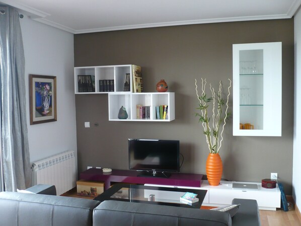 A living room with a television, bookshelves, a vase, and a sofa.