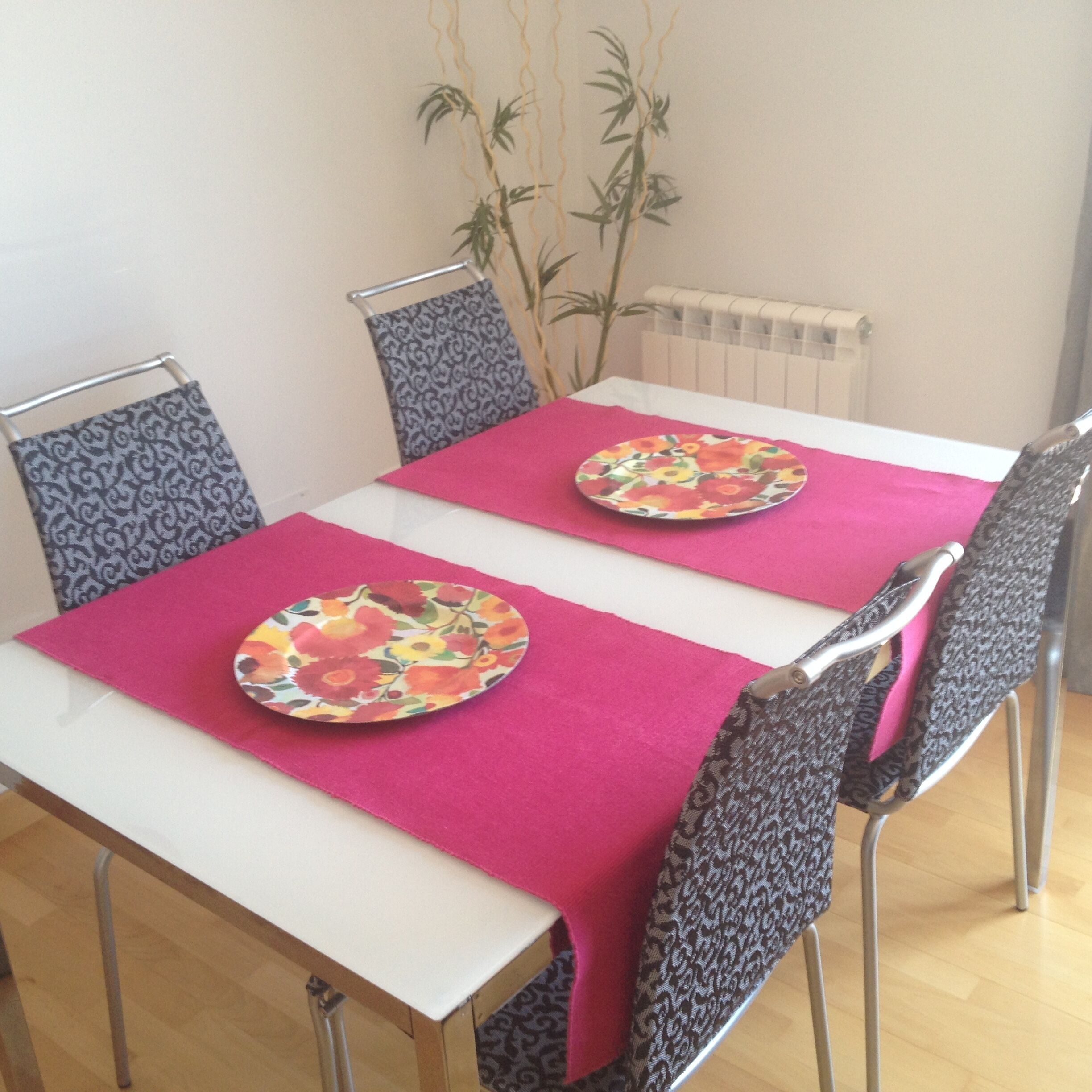 A dining table with two floral plates, a pink tablecloth, and patterned chairs.