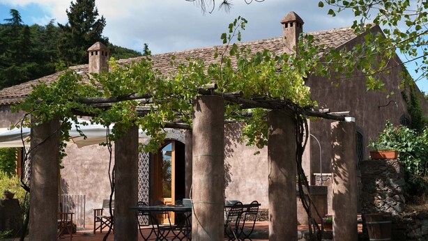 Ein rustikaler Sitzbereich im Freien mit einer Pergola, Steinpfeilern und einem Tisch mit Stühlen.