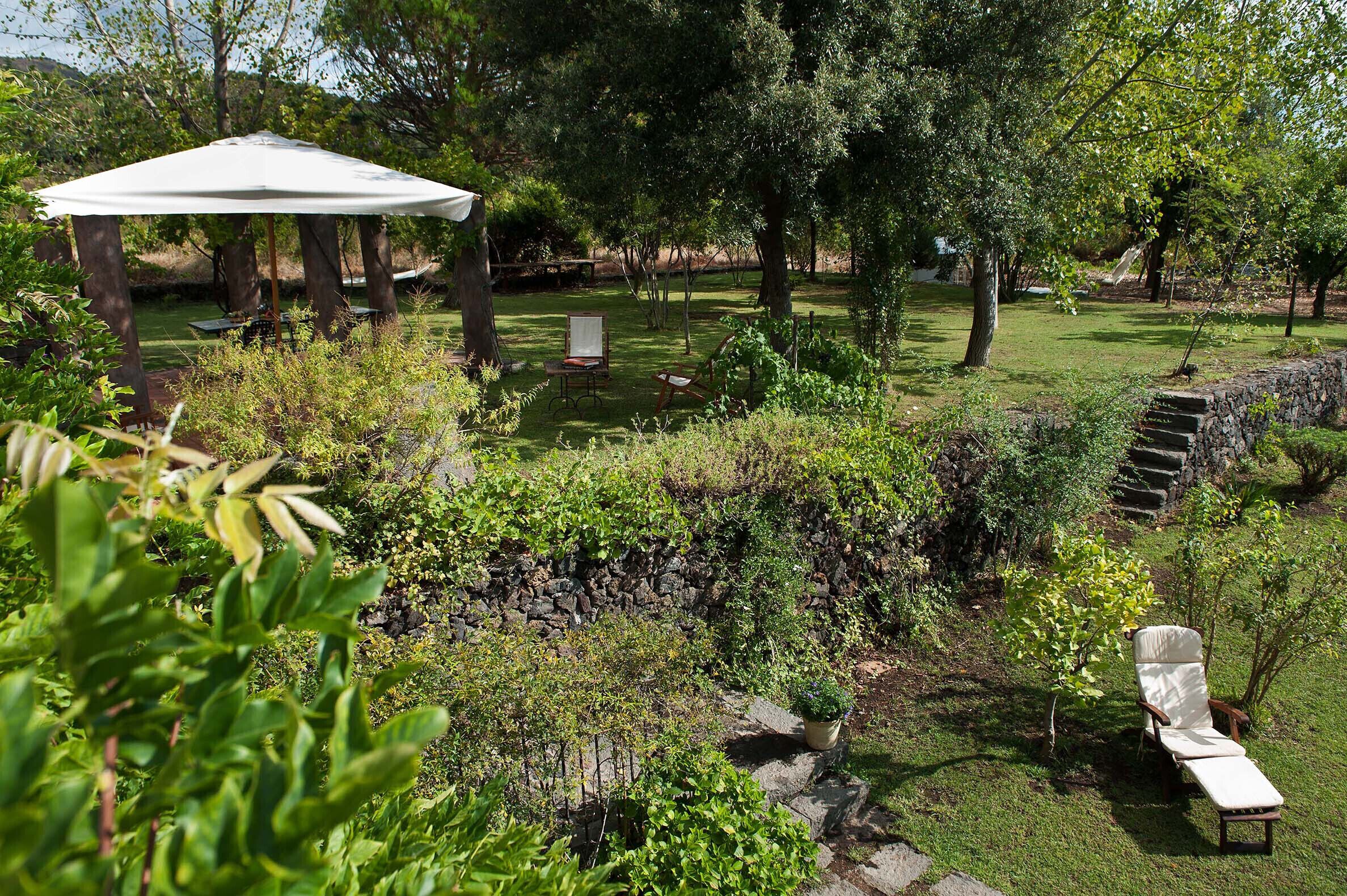 A garden with a gazebo, a stone wall, and a chair.