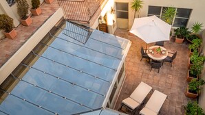 A rooftop patio with a glass ceiling, outdoor seating, and potted plants.