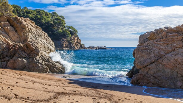 A rocky beach with clear blue water and a sandy shore.