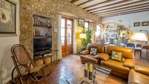 A cozy living room with a stone wall, wooden beams, a leather sofa, a television, and a bookshelf.