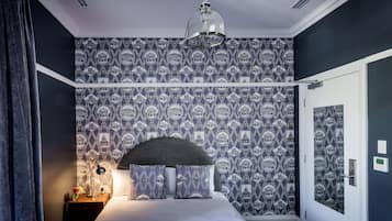 A bedroom with a patterned wallpaper, a bed with a grey headboard, a bedside lamp, and a hanging light fixture.