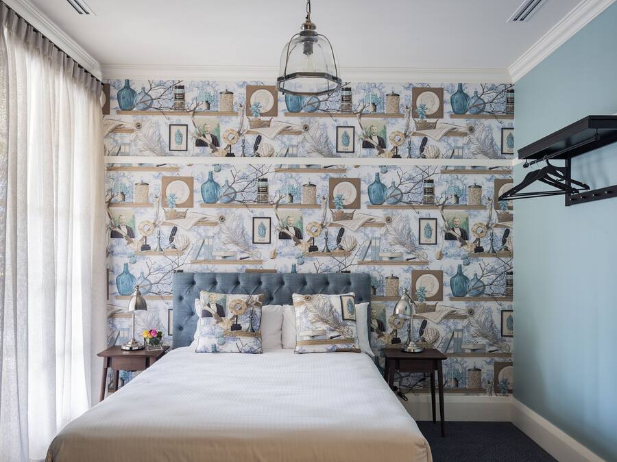 Un dormitorio con una cama grande, cabecera, mesita de noche, lámpara, lámpara colgante y estante en la pared.