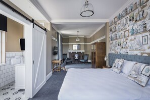 A hotel room with a large bed, a desk with two chairs, a bathroom with a white sink and toilet, and a wall decorated with framed pictures. - North Sydney Hotel (North Sydney)