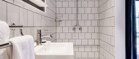 Un baño moderno con un lavamanos blanco, un espejo y una zona de ducha con azulejos blancos.