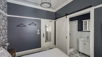Habitación de hotel con cama, armario, baño con lavabo y espejo, y una puerta que da a otra habitación.