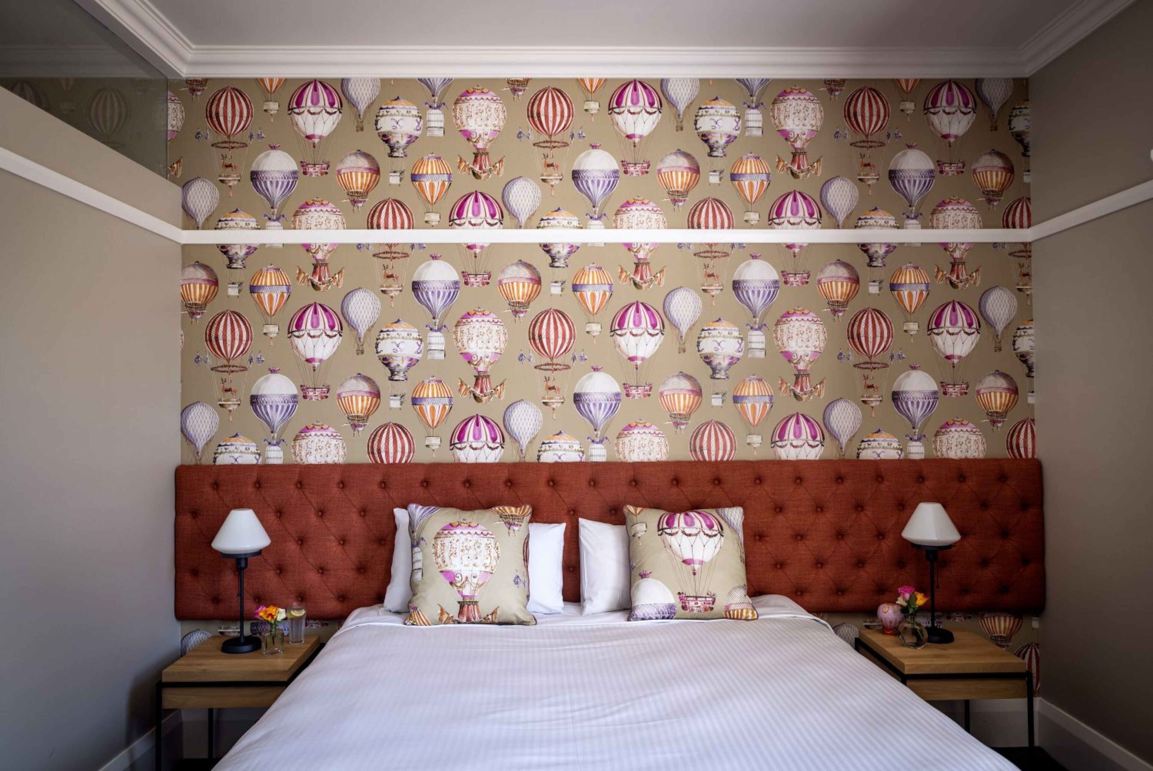 A hotel room with a large bed, a tufted headboard, and a patterned wallpaper featuring hot air balloons.