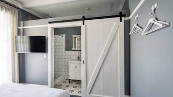 A hotel room with a bed, a sliding door leading to a bathroom, and a wall-mounted TV.