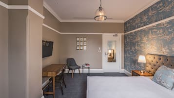 A hotel room with a bed, a desk, a chair, a small table, a lamp, and a ceiling fan.