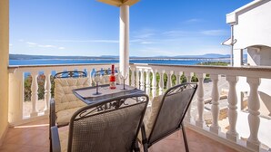 A balcony with a table and chairs, a bottle of wine, and a view of the sea and distant mountains.