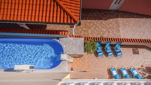 An aerial view of a rooftop pool area with a blue pool, lounge chairs, and a tiled roof.