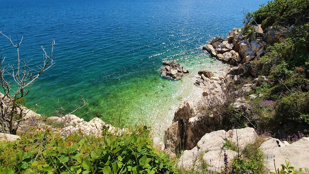 A coastal landscape with clear waters, rocky shoreline, and vegetation.