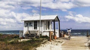 Ein kleines, weißes Strandhaus mit einstöckigem Bau, einer Veranda und einer Fahnenstange.