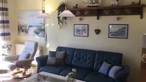 Ein Wohnzimmer mit einem blauen Sofa, einem Glastisch, einem Sessel und einem Regal mit Dekoration.