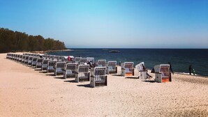 Ein Strand mit Reihen von Liegestühlen und Sonnenschirmen, einem klaren Himmel und dem Meer im Hintergrund.