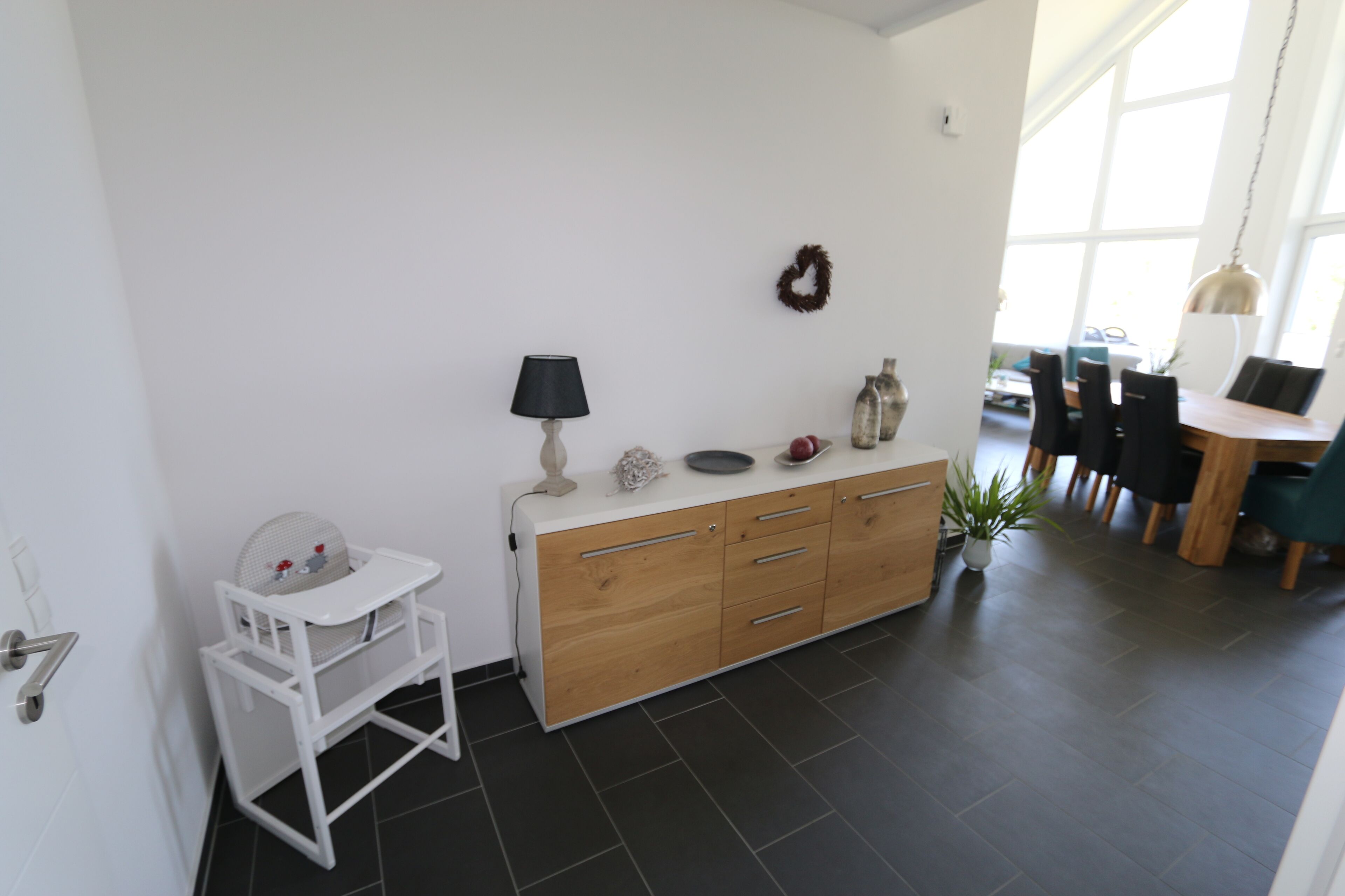A modern kitchen with a white countertop, wooden cabinets, a small white chair, and a dining area with a table and chairs.