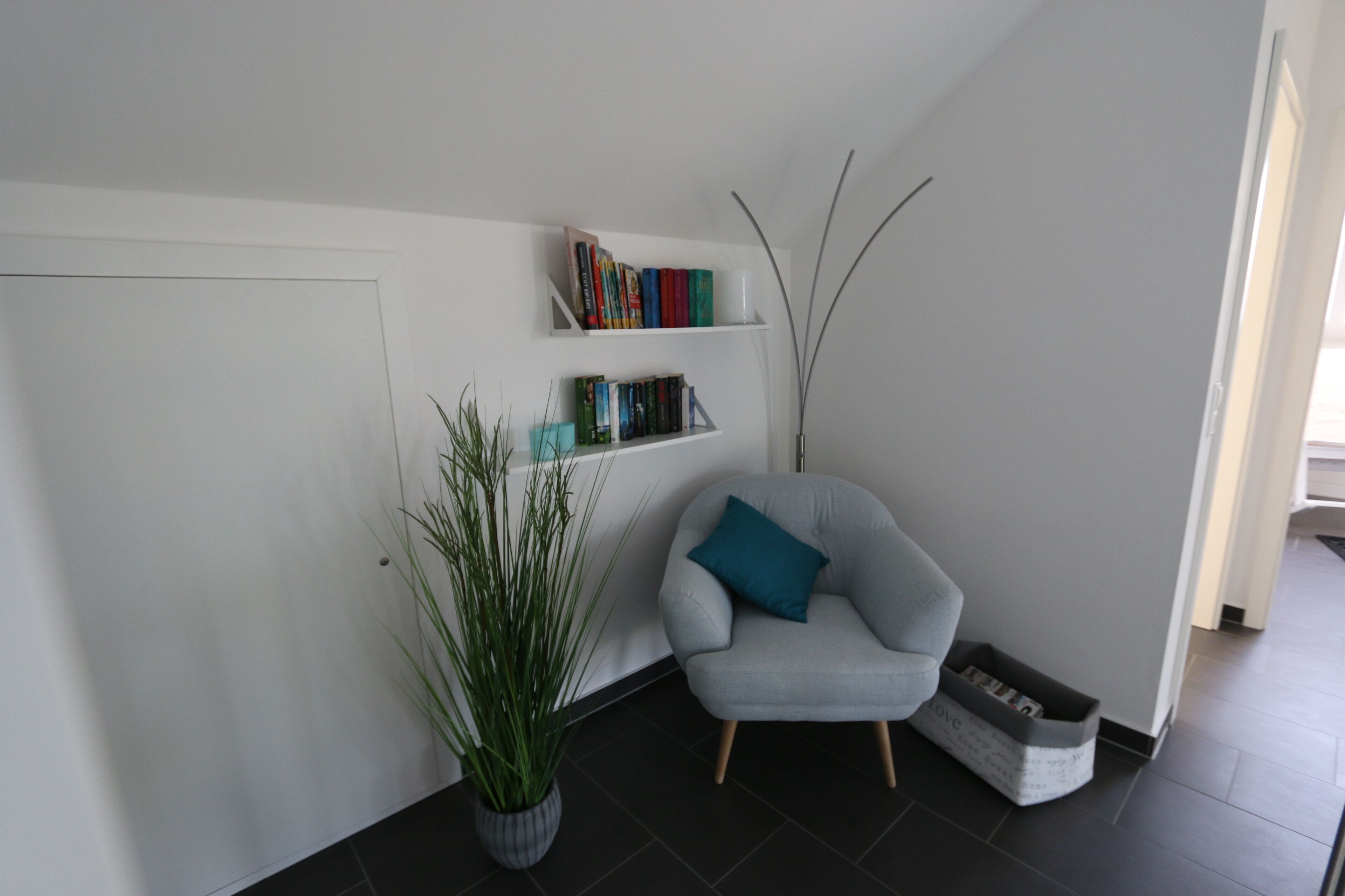 A modern living room with a grey armchair, a bookshelf, and a potted plant.