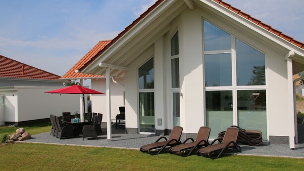 Et moderne hus med en patio, et spiseområde og et overdækket siddeområde med liggestole.