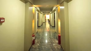 A hotel hallway with a marble floor, fire extinguishers, and a lighted exit sign. - Balibago Hotel (Angeles City)