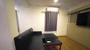 A living room with a black sofa, a wooden coffee table, and a flat-screen TV mounted on the wall. - Balibago Hotel (Angeles City)