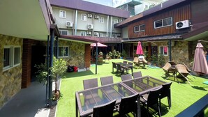A courtyard with a glass table and wicker chairs, surrounded by potted plants and a green artificial turf. - Balibago Hotel (Angeles City)