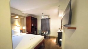 A hotel room with a bed, a desk, a chair, a TV, and a ceiling fan. - Balibago Hotel (Angeles City)