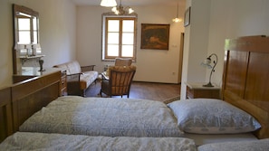 Une chambre à coucher avec deux lits, une commode en bois, une chaise, un bureau, une lampe et un tableau accroché au mur.