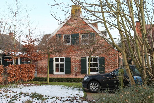 A brick house with green shutters and a car parked in front.