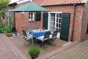 A brick patio with a table set for four, surrounded by chairs, under a green umbrella.