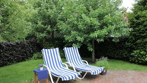 Two striped lounge chairs on a brick patio with a hedge and trees in the background. - Romantic Frisian house on the East Frisian coast (Krummhörn)