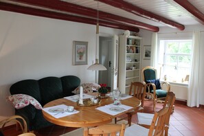 A dining area with a wooden table set for four, surrounded by wooden chairs. A green sofa and a wicker chair are also visible.